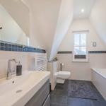 Badezimmer mit Dusche, Badewanne und Fenster unter Dachschrägen.