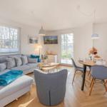 Wohn- und Essbereich mit Sofa, Tisch und Stühlen. Holzboden und große Fenster.