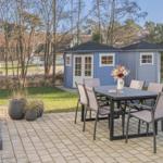 Terrasse mit Tisch und Stühlen, dahinter blaue Gartenhütten und Grünfläche.