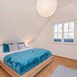 Schlafzimmer mit Holzbett, blauer Decke, Fenster und Deckenlampe.