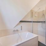Badezimmer mit Badewanne und Dusche unter schräger Decke.