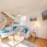 Wohnzimmer mit Sofa, Tisch und Treppenhaus. Wandbild und Fernseher an der Wand.