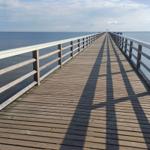 Holzbrücke führt über das Meer zu einem entfernten Tor.