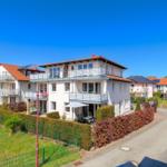 Modernes Mehrfamilienhaus mit Balkonen und Gartenbereich unter blauem Himmel.