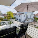 Terrasse mit Tisch, Stühlen und Sonnenschirm. Blick auf Wohnhäuser und Grünflächen.