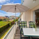 Terrasse mit Tisch, Stühlen und Sonnenschirm. Blick auf Garten und Nachbarhäuser.