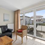 Wohnzimmer mit Sofa, Stuhl und Balkon mit Tisch und Sonnenschirm.