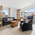 Wohnzimmer mit Ledersofa, Sessel und Terrasse. Holztisch und Gardinen.