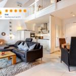 Wohnzimmer mit Sofa, Esstisch und Küche unter einer Galerie.