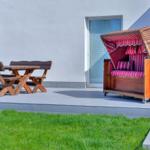 Terrasse mit Holztisch, Bänken und Strandkorb mit rotem Streifenstoff.