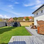 Hinterhof mit Terrasse, Garten und Holzstühlen. Weiße Hauswand und Holzgitter.