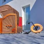 Außenterrasse mit Rattan-Sofa und Rettungsring. Hintergrund: weißes Haus mit Fenster.