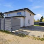Moderne Villa mit Garagenbereich und gepflastertem Hof. Umzäunt mit metallischem Zaun.