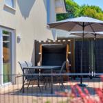 Terrace with table, chairs, and umbrellas. Backyard with fence and trees.