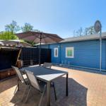 Terrace with table, chairs, and umbrellas next to blue house.