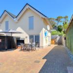 Haus mit Terrasse, Tisch, Stühlen und Sonnenschirmen. Hinterhof mit Holzzaun und Garten.