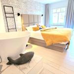 Schlafzimmer mit freistehender Badewanne und Holzboden. Wand mit Buchstabenmuster und Fenster mit Blick.
