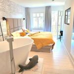 Schlafzimmer mit Badewanne, Bett und Balkon. Wand mit Text und Fischfigur.