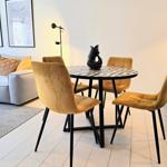 Runder Tisch mit vier Stühlen und Sofa im Hintergrund.