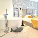 Schlafzimmer mit Badewanne, Textilmusterwand und gelbem Bettbezug.