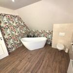 Badezimmer mit freistehender Badewanne, floraler Wand und Holzfußboden.