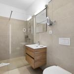 Bathroom with shower, sink, and toilet. Wooden shelf and mirror with lighting.