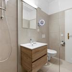 Bathroom with shower, sink and toilet. Wooden vanity and illuminated mirror.
