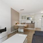 Wohnbereich mit Küche, Esstisch und Sofa. Weiße Möbel, Holzboden und Küchenschränke.