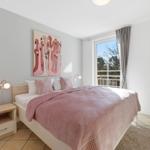 Schlafzimmer mit Bett, Wandbild und Fenster mit Blick auf Balkon.