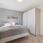 Schlafzimmer mit Bett, Schrank und Fenster. Wandbild mit bunten Flipflops.