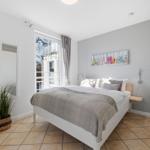 Schlafzimmer mit Bett, Fenster und Wandbild. Holzmöbel und Pflanze.