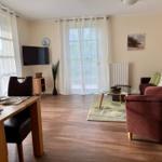 Wohn- und Essbereich mit Sofa, Tisch und TV. Holzboden und große Fenster.