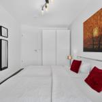 Schlafzimmer mit weißem Bett, roten Kissen und Wandbild.