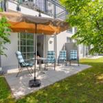 Terrasse mit Sonnenschirm, Tisch und vier Stühlen unter Bäumen.