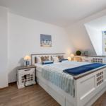 Schlafzimmer mit Dachschräge, Bett, Nachttisch, Fenster und Kleiderschrank.