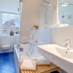 Badezimmer mit Dusche, Waschbecken und Toilette. Blaue Bodenfliesen und Spiegel.