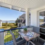 Terrasse mit Tisch und Stühlen. Blick auf Garten und Wasser.