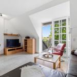 Living room with sofa, TV, and balcony access. Wooden furniture and red leather chairs.