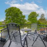 Terrace with table and chairs, view of green trees and blue sky.