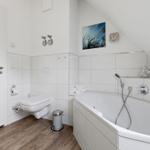 Bathroom with shower, bathtub, and toilet. Wooden floor and white tiles.