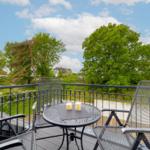Balcony with table and chairs, view of green trees and houses.