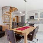 Dining area with wooden table, brown chairs, and kitchen with white cabinets.
