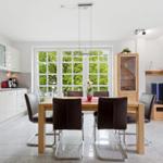 Modern kitchen with dining area and TV corner. Large windows with view of green trees.