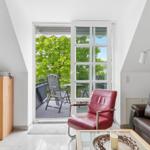 Living room with red armchair, brown sofa, and balcony with table and chairs.