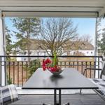 Balcony with table, chairs, and flowers. View of house and trees.