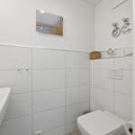 Bathroom with white tiled walls, sink, toilet, and wall picture.
