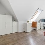 Room with sloped ceiling, white wardrobe, desk, and bed with pink bedding.