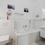Bath with bathtub, sink, and toilet. White tiles and mirror.
