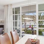 Dining area with view of balcony and garden. Table with fruit bowl and chairs.