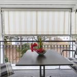 Balcony with table, chairs, and flowers. View of green areas and buildings.